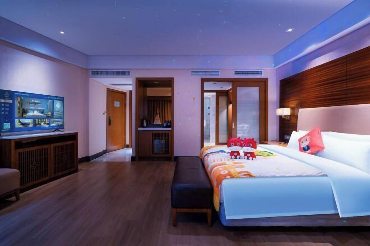 A hotel room with a bed, a TV, a desk, and a bench.
