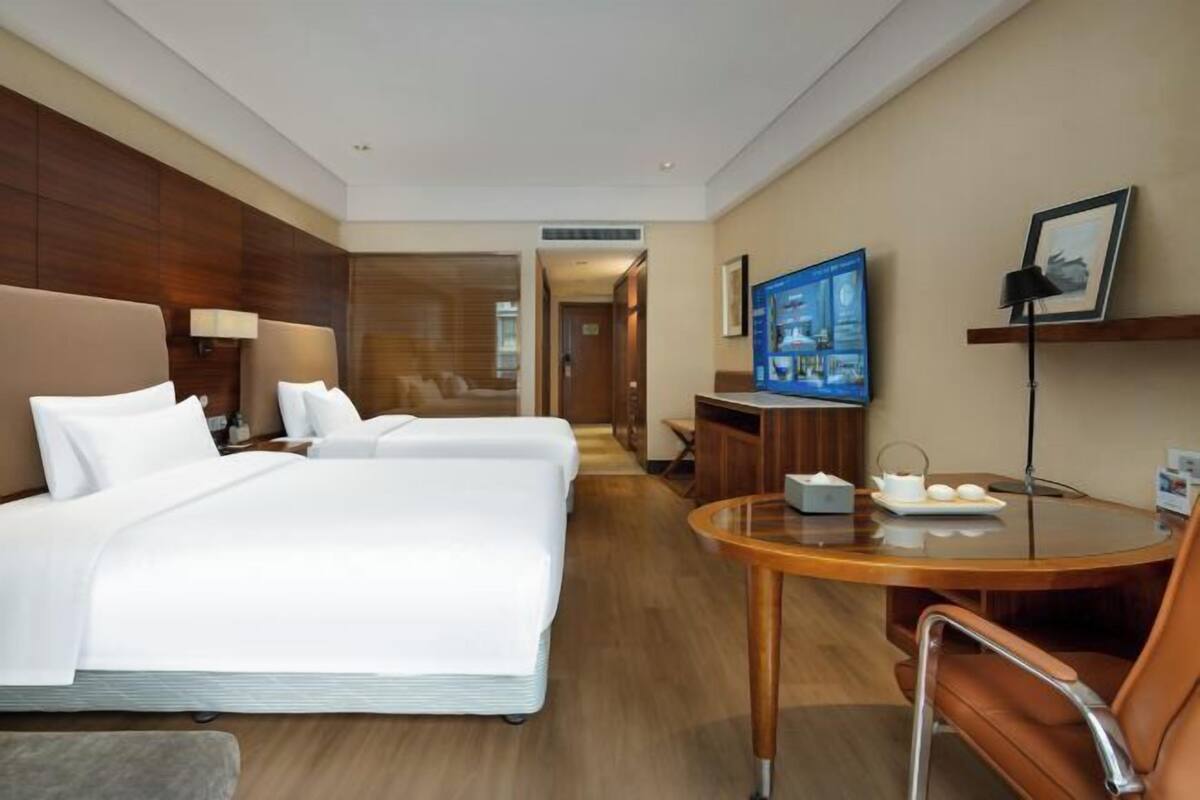 A hotel room with two beds, a TV, a desk with a chair, and a wooden floor.