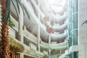 Un atrium à plusieurs niveaux, doté d’un escalier central, de palmiers et de décorations florales suspendues.
