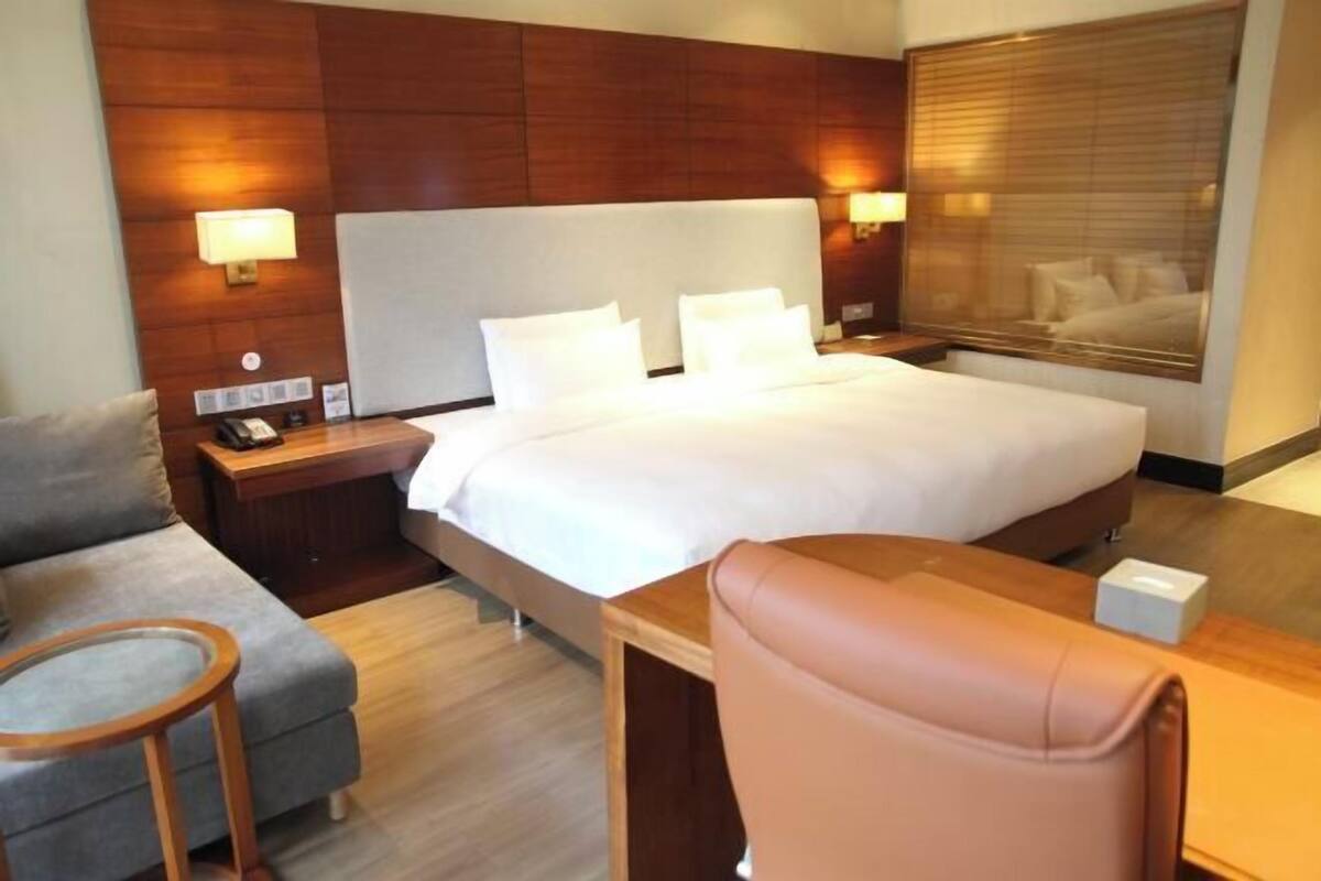 A hotel room with a large bed, a sofa, a chair, a desk, and a nightstand with a lamp.