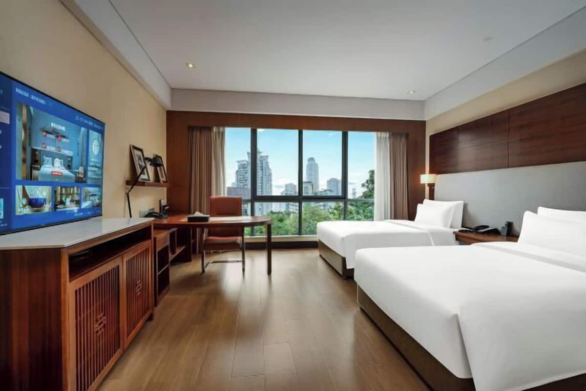 A hotel room with a large TV, two beds, a desk, and a view of the city.