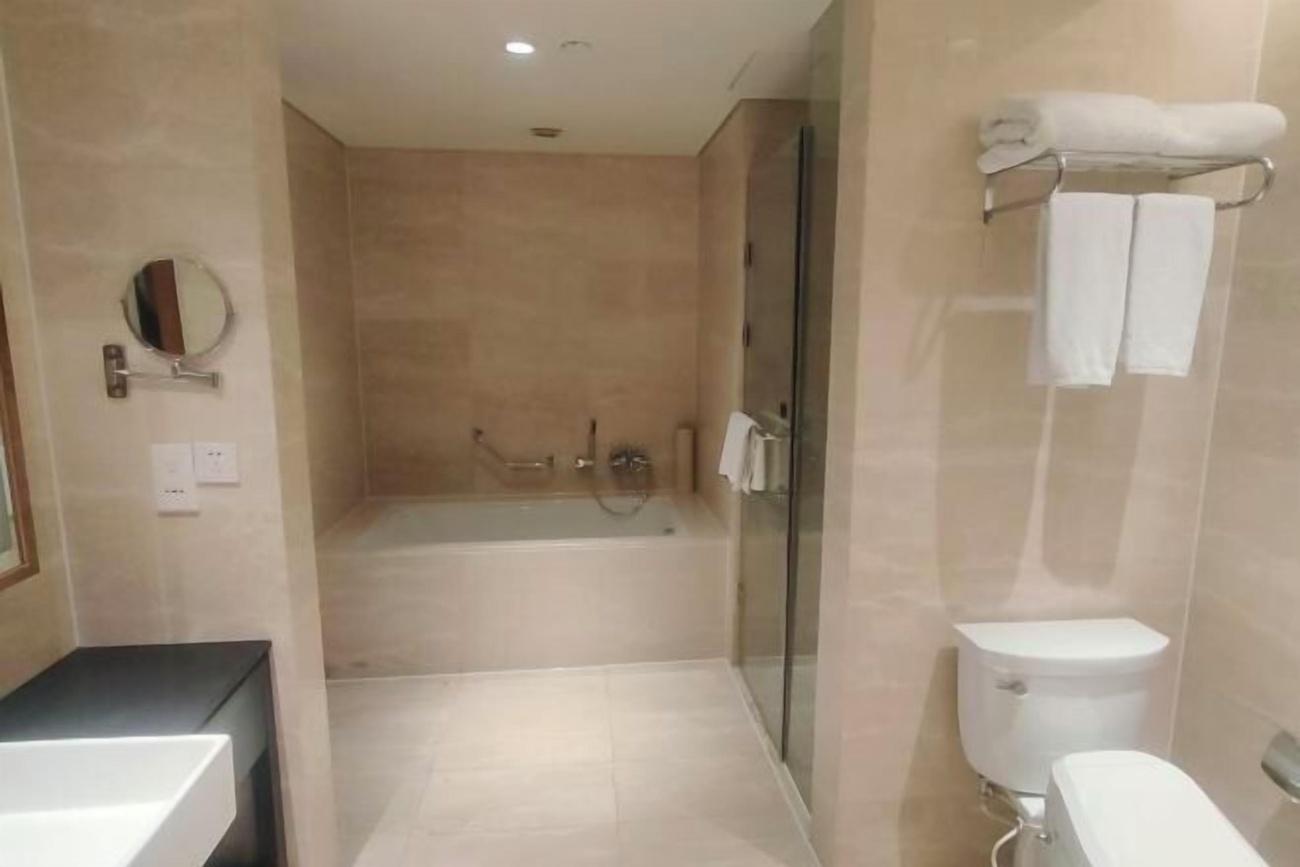 A modern bathroom with a bathtub, toilet, and glass shower enclosure.