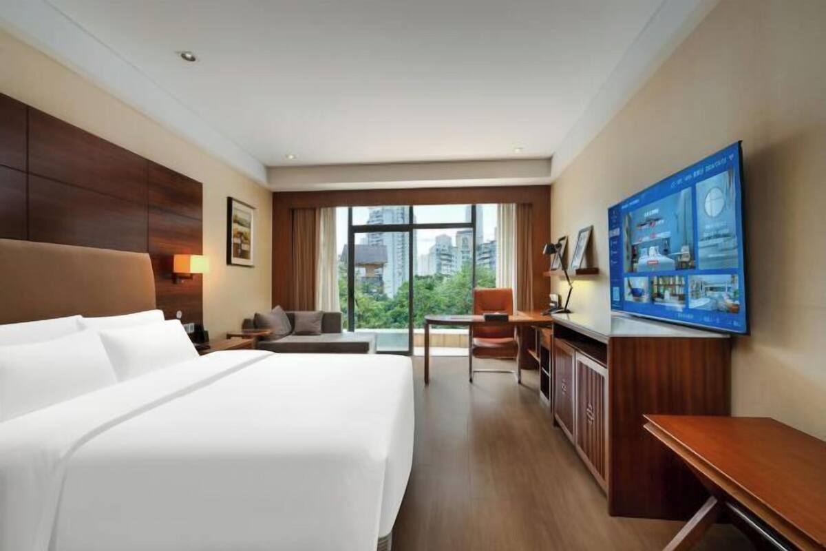 A hotel room with a large bed, a desk, a chair, and a television.