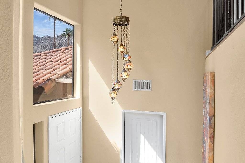 A hallway with a decorative hanging light fixture, a window with a view of a tiled roof, and a door.