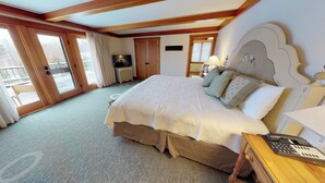A hotel room with a large bed, a wooden headboard, a desk with a telephone, and a television on a nightstand.