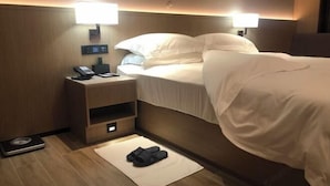 Et hotelværelse med en seng, sengeborde med lamper, et telefon og en vægt, samt en måtte med slippers.