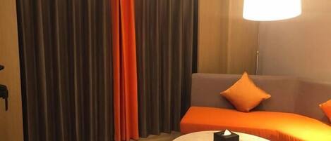 A room with a sofa and a round table, curtains, and a hanging light fixture.