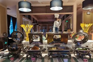 A buffet setup with multiple serving stations, a chef, and various food items. - Qionghai Changlong Hotel (Yinhai Zaliang Street) (Qionghai)