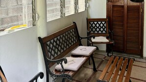 A covered outdoor seating area with two benches and a table, wooden ceiling, and a view of a building through the windows. - The breeze from Gros Morne to Deshaies (Deshaies)