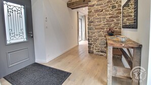 A hallway with a stone wall, a wooden table with items on it, and a door with a decorative window.