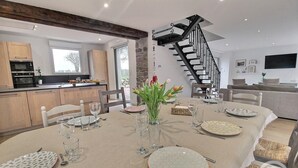 A dining area with a table set for four, a kitchen in the background, and a staircase leading to an upper level.