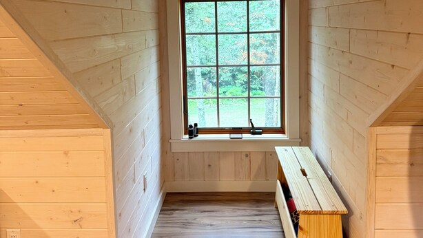 Un dormitorio de ático con piso de madera, un gran ventanal y una banca.
