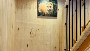 Interior de madera con una escalera de madera, un cuadro enmarcado de un zorro y una lámpara en el techo.