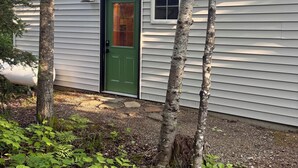 Una casa de un piso con una puerta verde, un ventanal pequeño y una chimenea.
