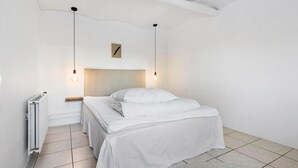 Une chambre à coucher minimaliste avec un lit simple, du linge de lit blanc et des lampes suspendues.