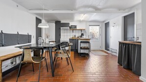 Une cuisine moderne avec un coin repas, dotée d’un sol en briques, de murs blancs et d’une grande fenêtre.
