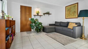 Un salon avec un canapé gris, une bibliothèque, une plante en pot, une carte accrochée au mur et une lampe.
