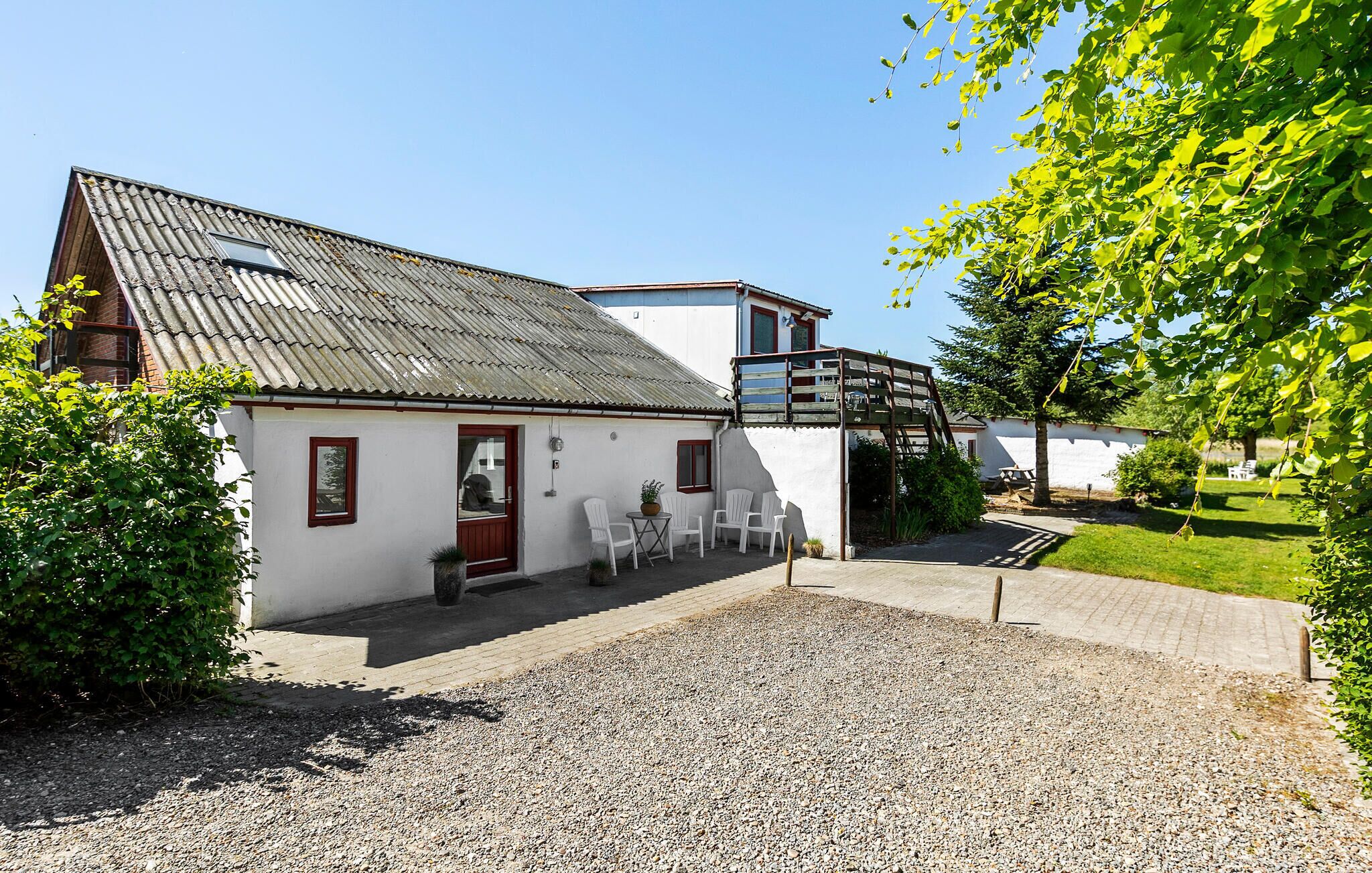 A white building with a red door, a gravel driveway, and white chairs outside.
