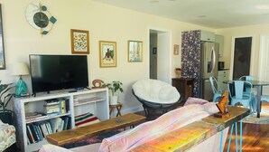 Una sala de estar con un sofá, un televisor, una estantería, una silla y un comedor con sillas y una mesa.