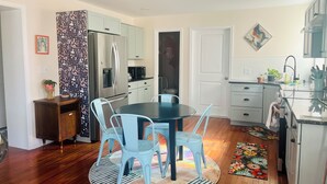 Una cocina moderna con una isla central, armarios blancos y un comedor con sillas azules.