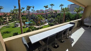 A balcony with a table and chairs, overlooking a pool area with palm trees and a building in the background. - 1 Bdrm, 2 Baths!!!! This is a larger 2 bdrm, chng'd to a 1 Bdrm!   MUCH LARGER!! (Cabo San Lucas)
