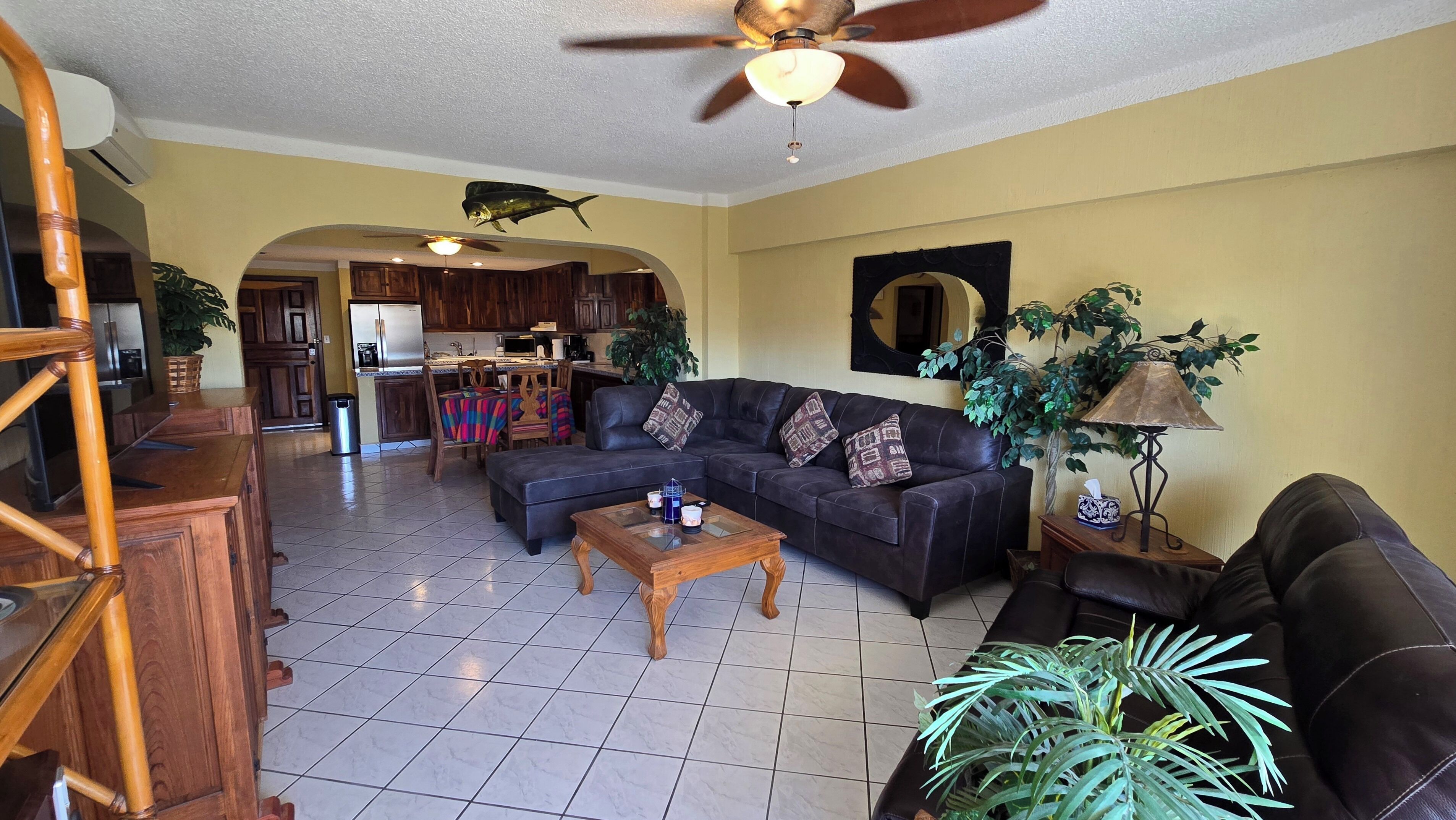 A spacious living room with a dark leather sofa, a wooden coffee table, and a ceiling fan.