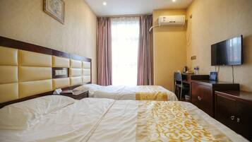 A hotel room with two beds, a desk, a chair, a TV, and an air conditioning unit.