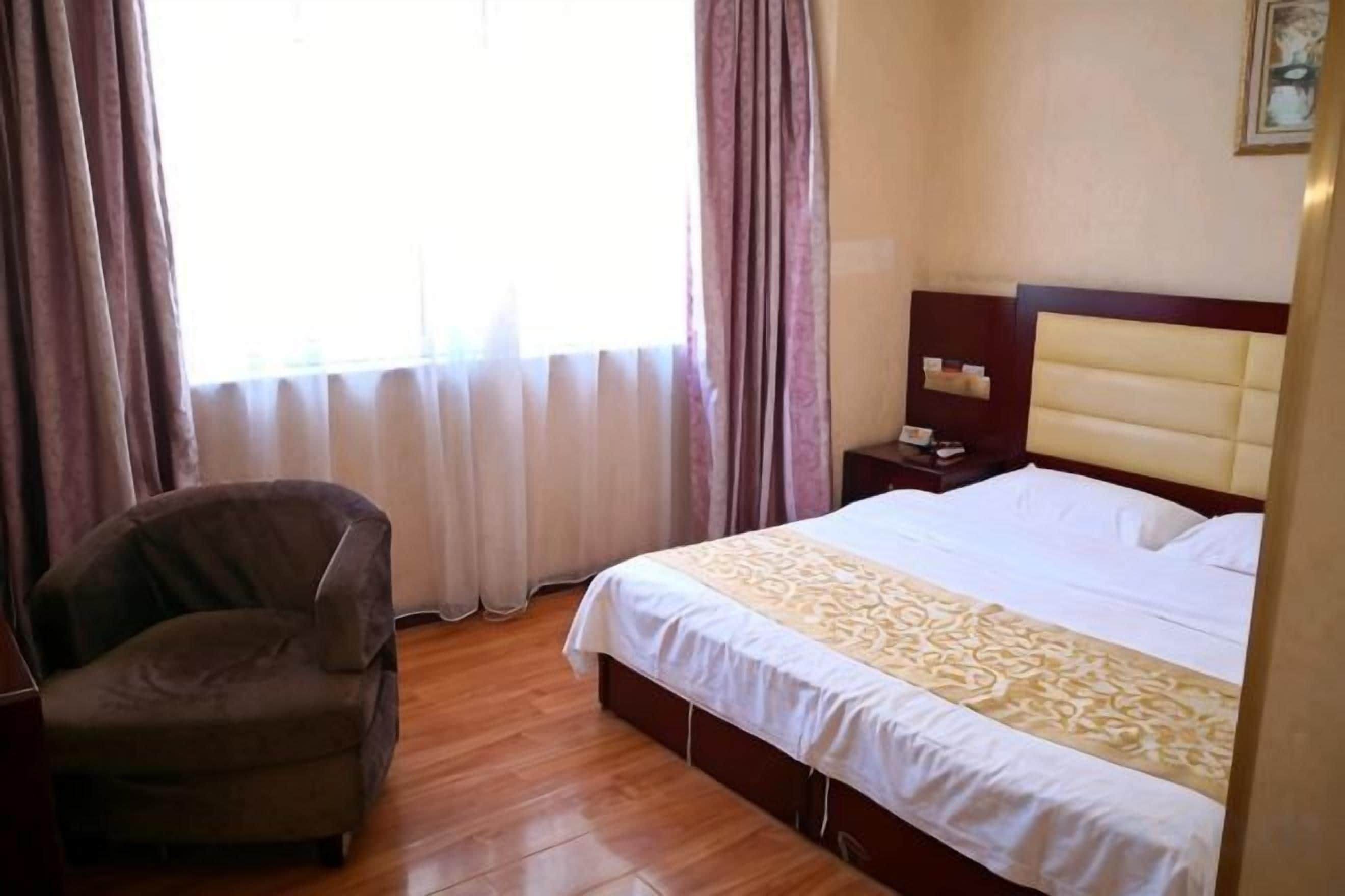 A hotel room with a bed, a chair, a nightstand, and a window with curtains.
