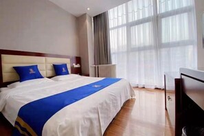 Una habitació d'hotel amb un llit gran, un panell de fusta al capçal, una taula de nit, una televisió i una finestra amb cortines.