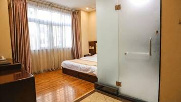 A hotel room with a bed, a wardrobe, a desk, and a window with curtains.