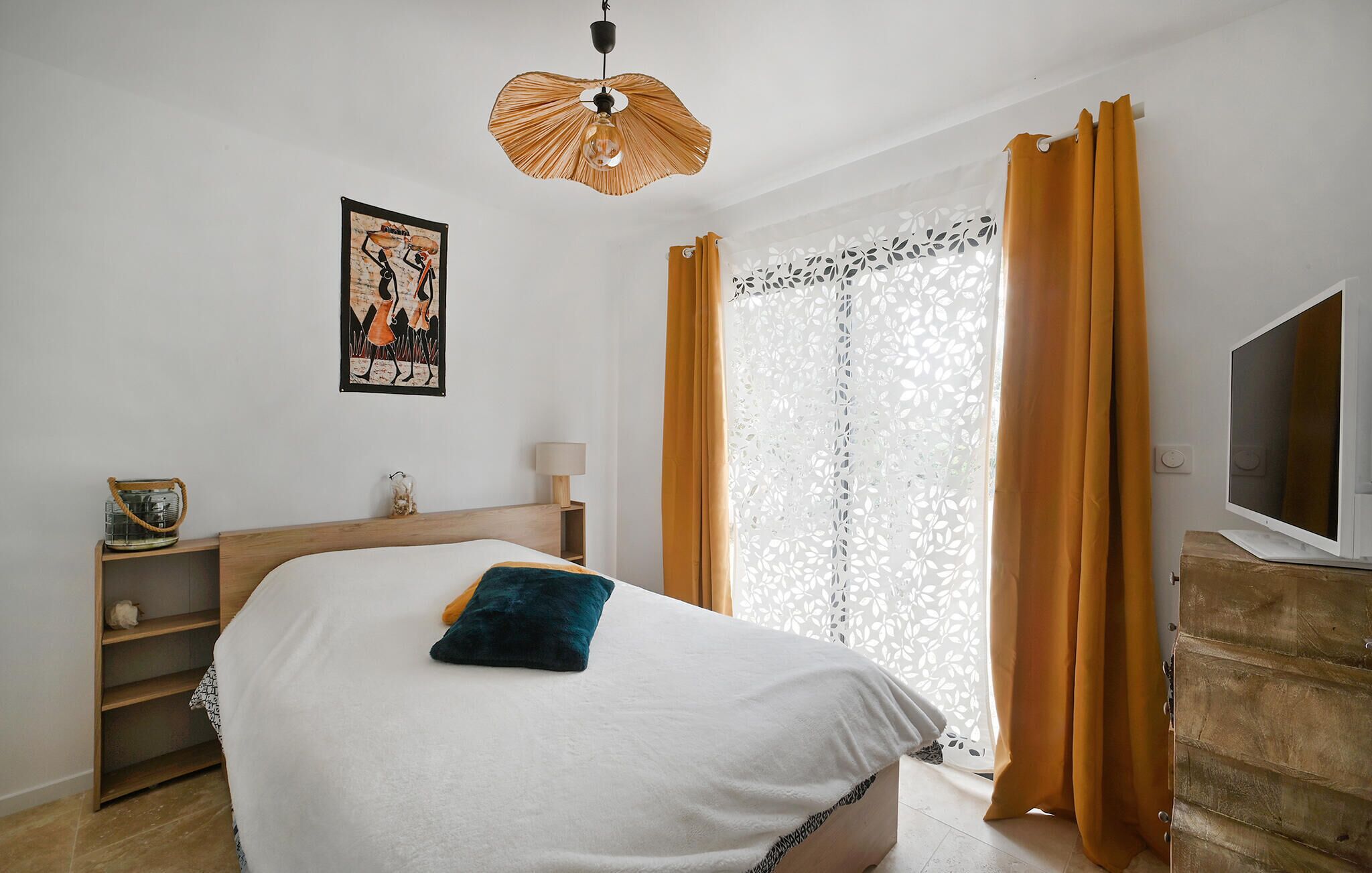 Un dormitorio con cama, mesita de noche, lámpara, televisión y ventana con cortinas.