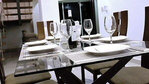A dining table set with plates, glasses, and a bottle, with chairs around it. - Sejour's Penthouse (Santo Domingo Este)