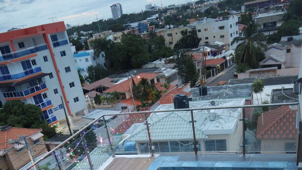 A rooftop swimming pool with a wooden deck and stairs leading to it, surrounded by buildings. - Sejour's Penthouse (Santo Domingo Este)