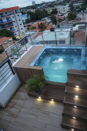 Une piscine sur le toit, dotée d’une terrasse en bois et d’un escalier menant à l’eau, le tout entouré d’immeubles.