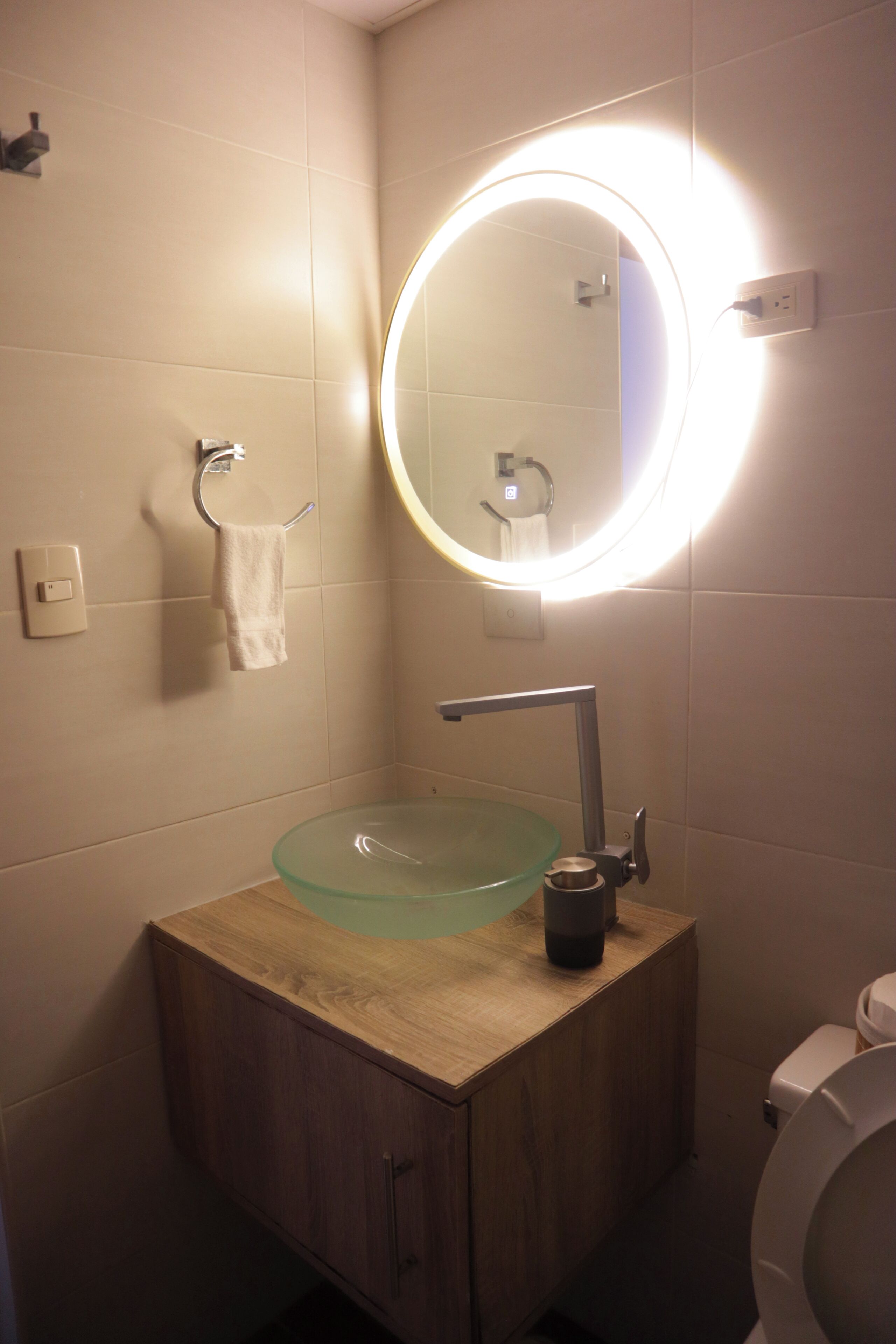 A bathroom with a round mirror, a glass sink, a wooden cabinet, and a toilet.