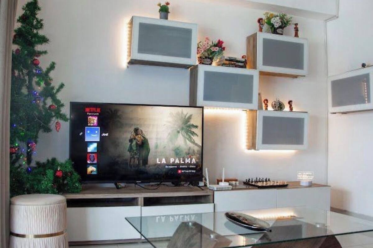 Una sala de estar moderna con un televisor de pantalla plana, una mesa de centro de vidrio y un árbol de Navidad decorativo.
