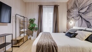 Makuuhuoneessa on sänky, televisio, vaatekaappi, huonekasvi ja seinä, jossa on lehtikuviota.