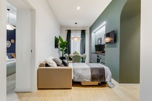 A compact bedroom with a bed, a small seating area, a dining table, and a TV mounted on the wall.