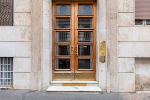 A double wooden door with glass panels, a metal gate, and a small step leading to the entrance.