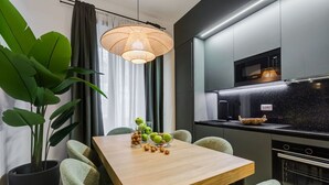 Moderni keittiö, jossa on sisäänrakennettu mikroaaltouuni, musta työtaso sekä ruokailutila, jossa on puinen pöytä ja vihreät tuolit.