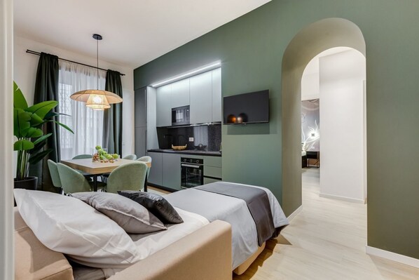 A modern apartment with a dining area, kitchenette, and a living space with a sofa and a TV.