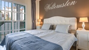 Une chambre avec un grand lit, deux tables de chevet, une fenêtre avec des rideaux et un mur sur lequel est écrit le mot « Wellerusten ».