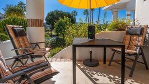 Un espace extérieur aménagé avec deux fauteuils confortables et une table, un parasol jaune, et une vue sur une piscine et de la verdure.