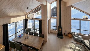 A wooden interior with a dining table, chairs, a fireplace, and large windows offering a view of a snowy landscape. - Gorgeous home in Kvam with sauna (Kvam)