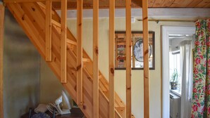 Eine Holztreppe führt zu einer oberen Etage, ein gerahmtes Bild an der Wand und eine Tür mit floralen Vorhängen.