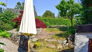 Ein Garten mit weißem Sonnenschirm, Steinmauern und verschiedenen Pflanzen.