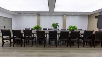 Un salón de conferencias con una larga mesa, sillas, plantas en macetas y un televisor de pantalla plana.