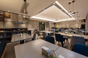 Un comedor moderno con varias mesas y sillas, una zona de cocina con electrodomésticos e iluminación colgante.