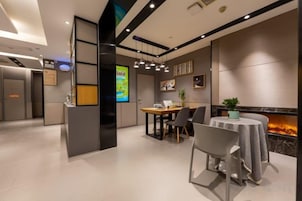 Un moderno vestíbulo de hotel con una recepción, un área de comedor con chimenea y una pantalla digital que muestra información.