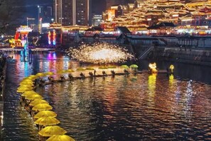 A river with illuminated boats and a traditional building complex in the background. - Homeinn Selected Hotel (Enshi Tusi City ) (Enshi City)